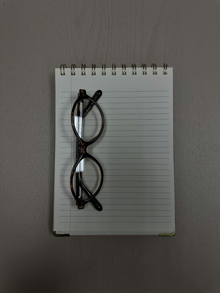 Óculos de grau de armação preta sobre um caderno espiral em cima da mesa