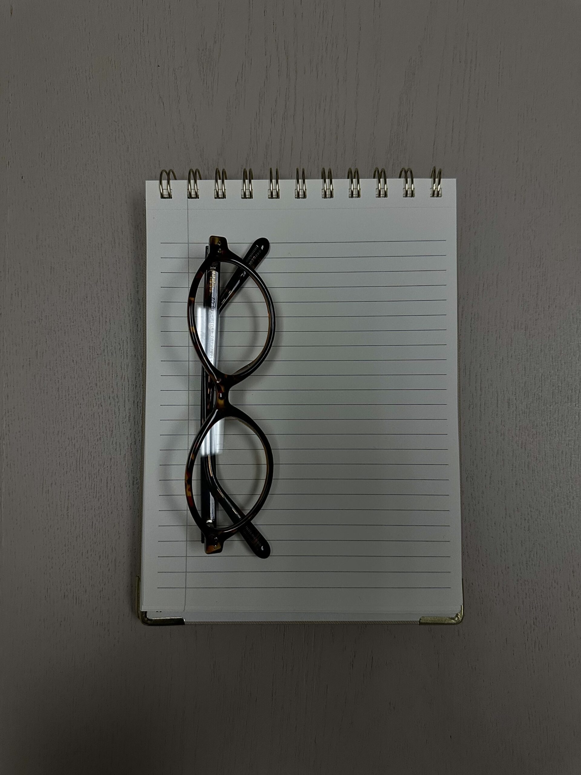 Óculos de grau de armação preta sobre um caderno espiral em cima da mesa