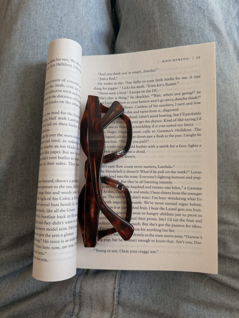 Óculos de grau de armação marrom tartaruga apoiado nas páginas de um livro aberto