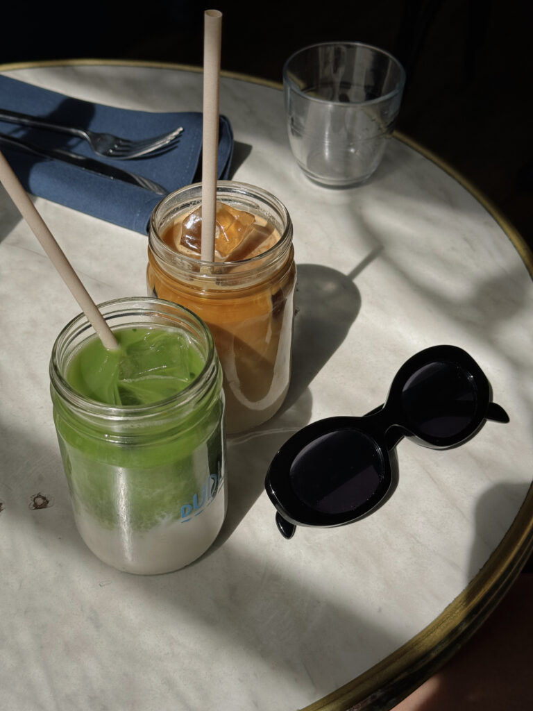 Óculos de sol preto sobre uma mesa ao ar livre, ao lado de copos de suco verde e laranja
